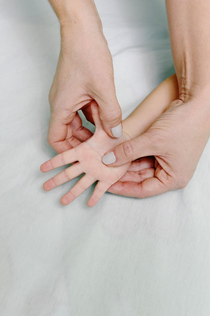 Close-up of a child's hand being gently massaged by an adult's hands on a soft surface.